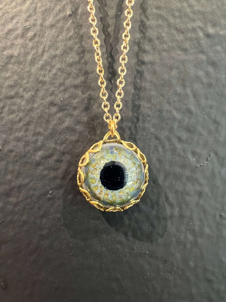 Handblown blue borosilicate glass eye caged in vintage brass filigree and hanging on a brass chain.