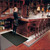 Woman in restaurant uniform standing to the side of a bar retrieving a tray of wine while standing on large, black, Cushion Select mat.