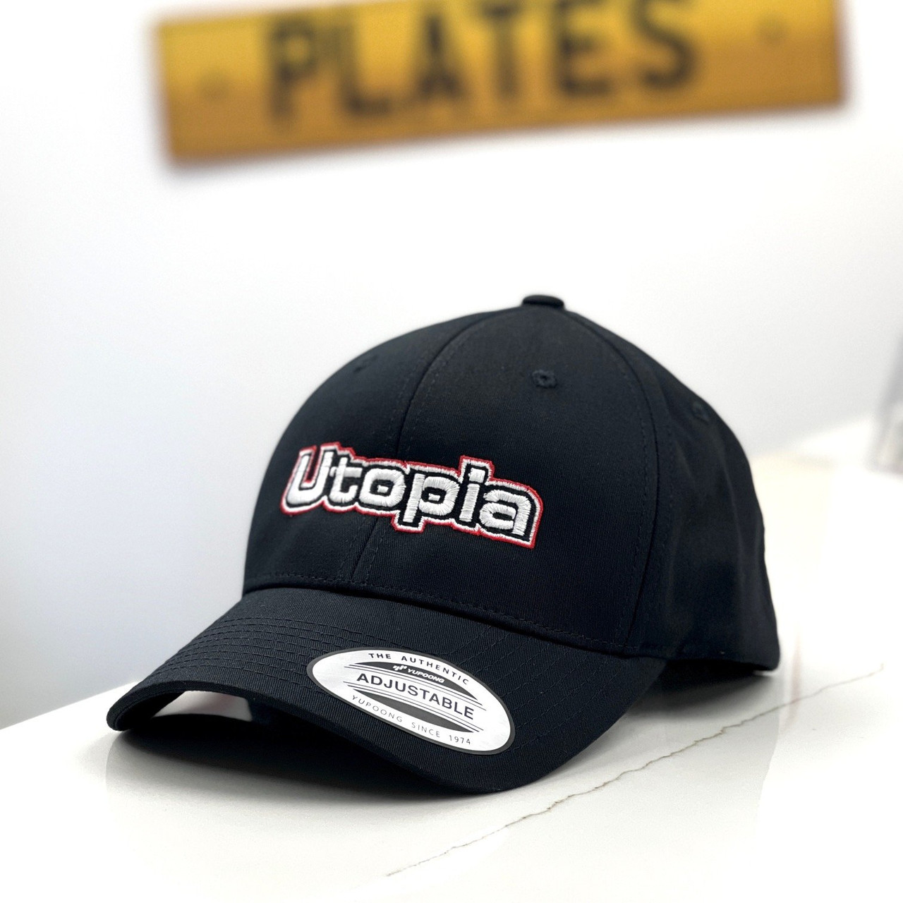 The Utopia Plates branded logo black cap with the company logo in the background