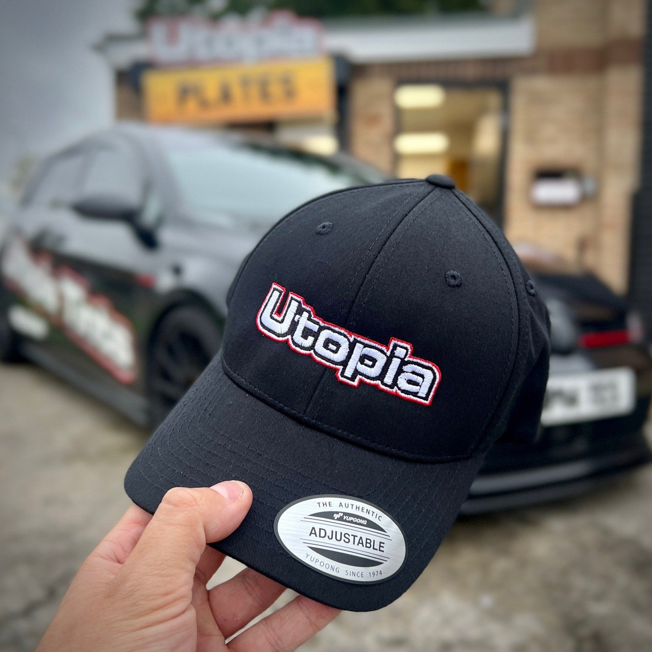 Black Utopia branded cap in front of a Golf GTi and the Utopia Plates shop in Durham