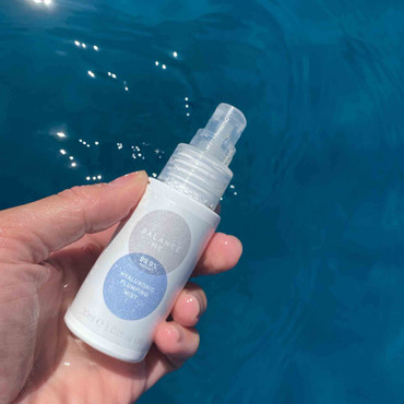 Balance Me Hyaluronic Plumping Mist 30ml being held above some beautiful blue water