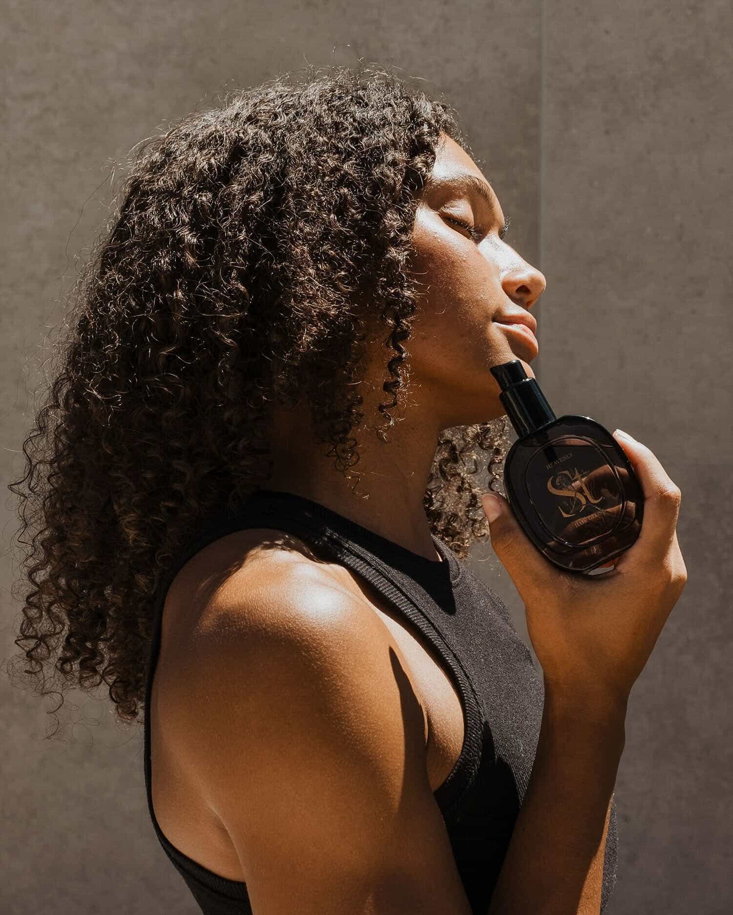 Side profile of woman holding Seint Heavnly Hair Gloss product.