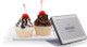 A clear L-style smart label stand displaying a digital retail label next to two cupcakes on a white background.