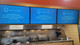 Three 75" LG Lite Duty Smart Screens mounted above a service counter, displaying WAND digital signage content.
