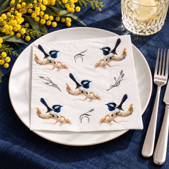 Australian Blue Wren paper napkin displayed on a blue tablecloth with wattle flowers, crystal glassware and elegant silver