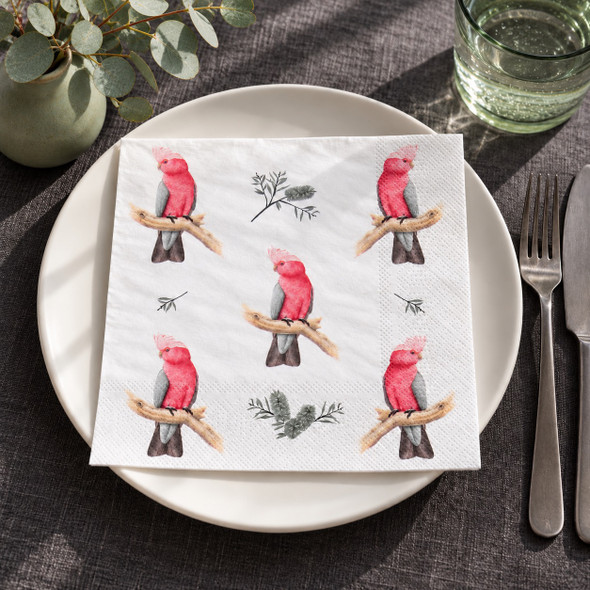 Australian Pink Galah paper napkin displayed on a white dinner plate with charcoal grey table linen, eucalyptus greenery, green glassware and silver cutlery