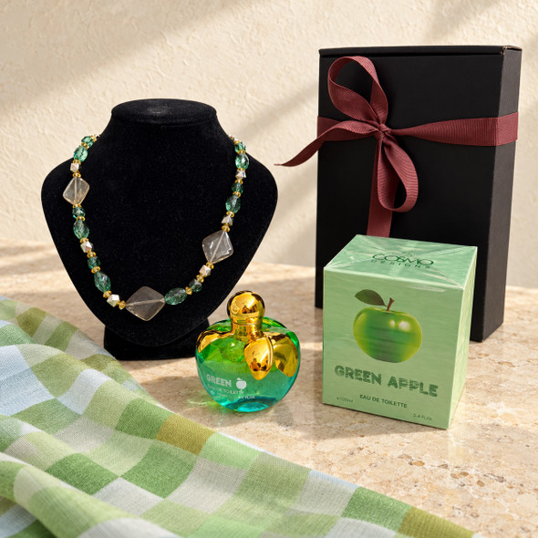 Perfume close-up: Green Apple Eau de Toilette 100ml in an apple-shaped bottle beside its carton, coordinating necklace and green checked scarf.