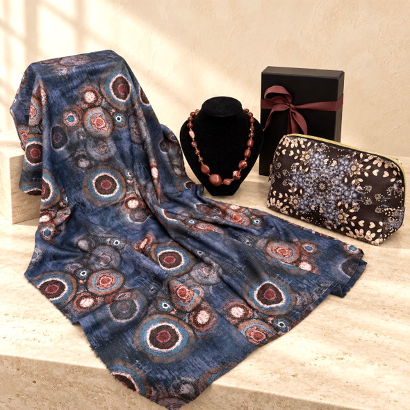 Blue abstract print shawl with a brown La Garde Freinet necklace, patterned cosmetic bag and black gift box with burgundy ribbon.