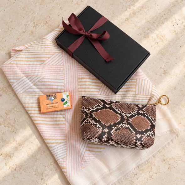 Geometric scarf, small snakeskin-print cosmetic bag and Le Petit Marseillais orange blossom soap arranged with a ribbon-tied gift box.