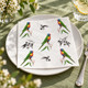 Australian Rainbow Lorikeet paper napkin displayed on a white dinner plate with sage green table linen, white flowers, crystal glassware and silver cutlery