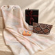Main image: Ivory scarf with peach and beige geometric stripes, snakeskin-print cosmetic bag and orange blossom French soap beside a black gift box with burgundy ribbon.