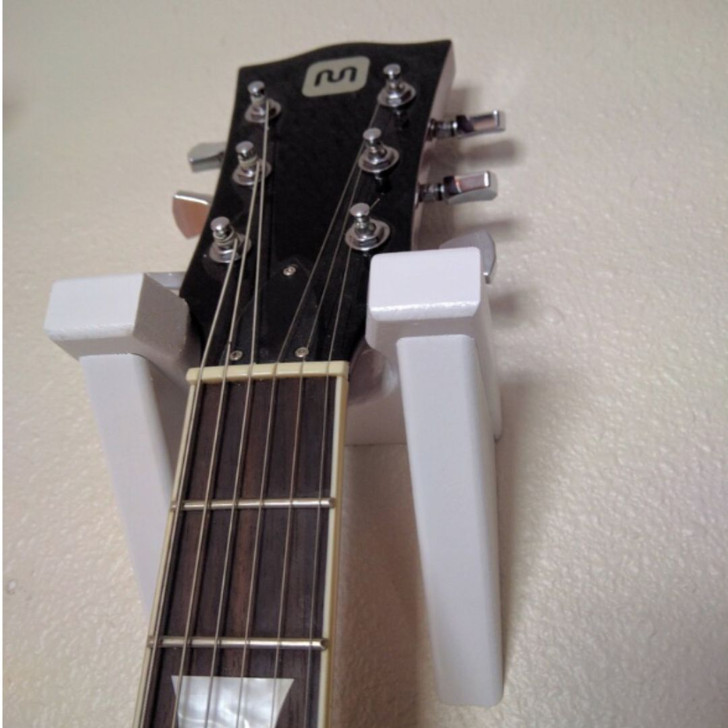 White classical guitar hanger mounted on wall with guitar hanging