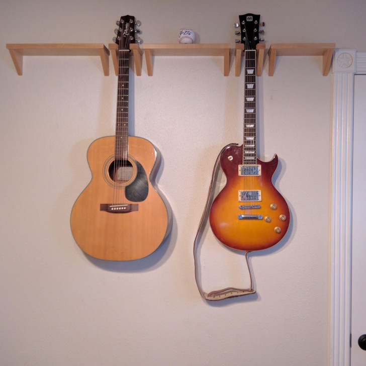Two maple guitar hangers installed on wall with guitars next to coordinating maple shelves