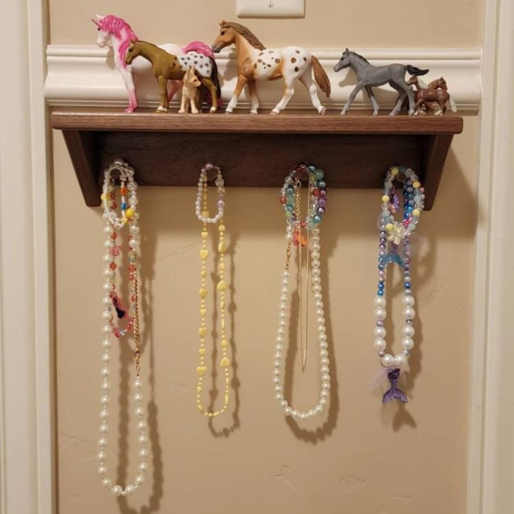 16 inch walnut shelf with 4 pegs, shown on the wall with horses on top and necklaces hanging on pegs