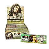BOB Marley Papers Bob Marley Cigarette Papers Organic Hemp 1 1/4 25Ct, display box containing multiple packs of rolling papers with Bob Marley's image and logo, and a single pack of organic hemp rolling papers with Bob Marley's face and a green background.