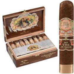 My Father Cigars Mf The Judge Grand Robusto 23 Ct. Box, an open wooden box containing 23 cigars with colorful branding and artwork, alongside a single, large, hand-rolled cigar with a decorative band.