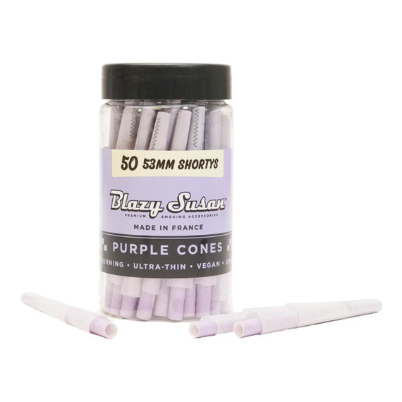 Blazy Susan 53Mm Shorty Purple Pre-Rolled Cones 50Ct, transparent container with purple pre-rolled cones for smoking, with a few cones placed in front of the container.