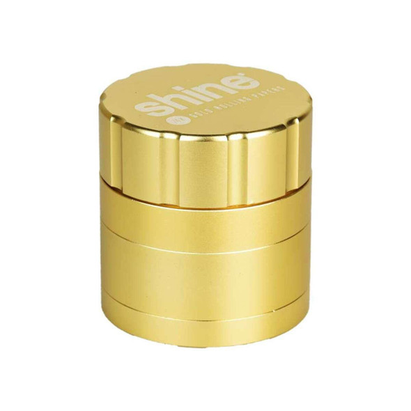 Shine Rolling Paper Shine Gold Grinder - 4pc, 2-inch gold-colored herb grinder with a sleek, compact design and branded lid for grinding herbs.