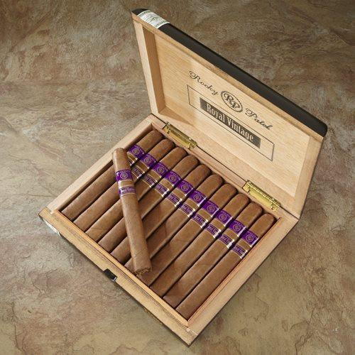 Rocky Patel Royal Vintage Cigars, open wooden box filled with neatly arranged cigars and one cigar placed on top, inside a wooden box with branding and logo.