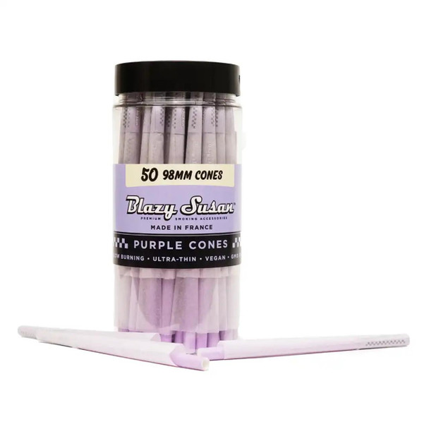 Blazy Susan 98Mm Purple Pre-Rolled Cones 50Ct, transparent plastic container filled with purple pre-rolled cones and two cones lying in front of it.