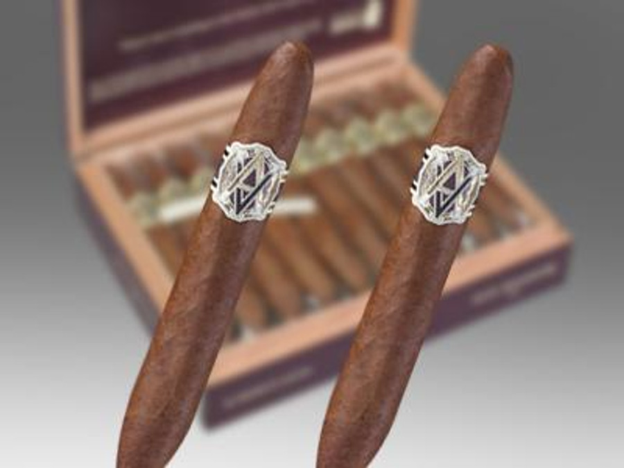 AVO Cigars Heritage Short Robusto 20 Ct. Box 4.00X56, two cigars with silver bands and brown wrappers, with an open box containing additional cigars in the background.