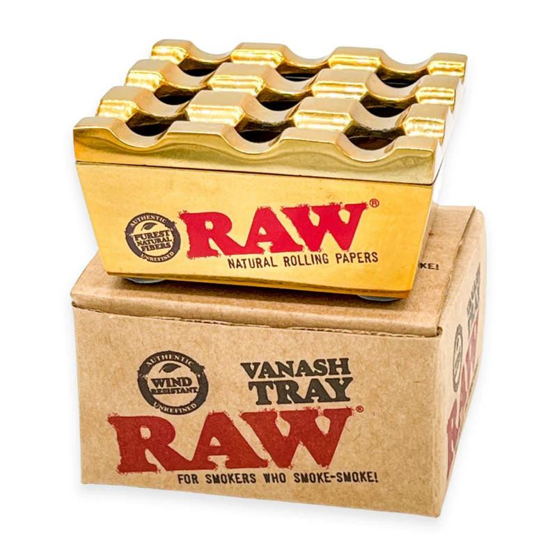 RAW Vanash Tray, metallic gold rolling paper tray with wavy slots for rolling papers, placed on RAW branded cardboard box for smokers.