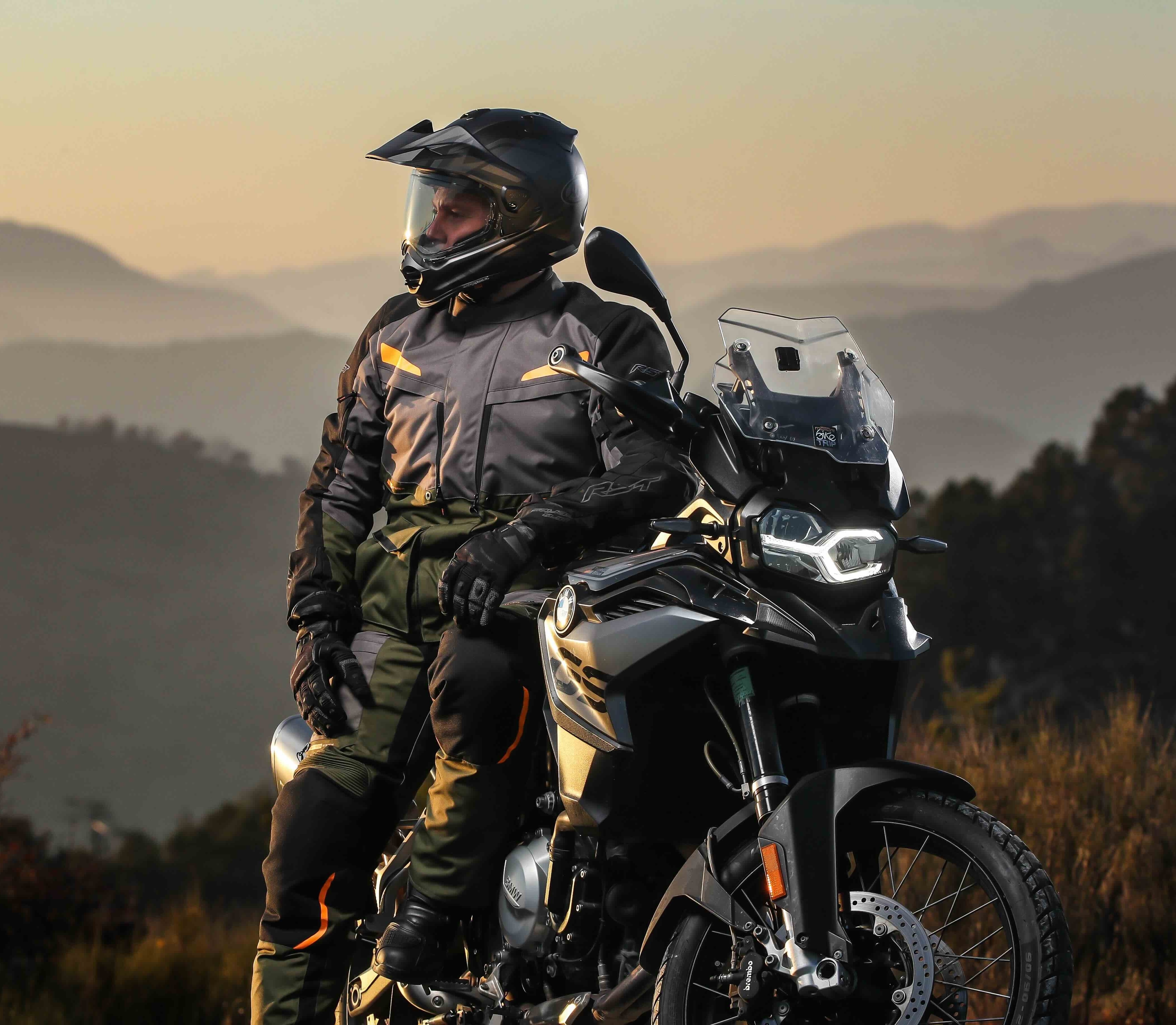 Image of an adventure motorcyclist leaning against his bike as the sun sets
