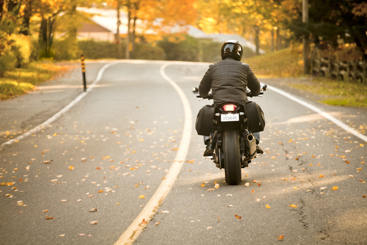 person riding a motorcycle down a road in the fall