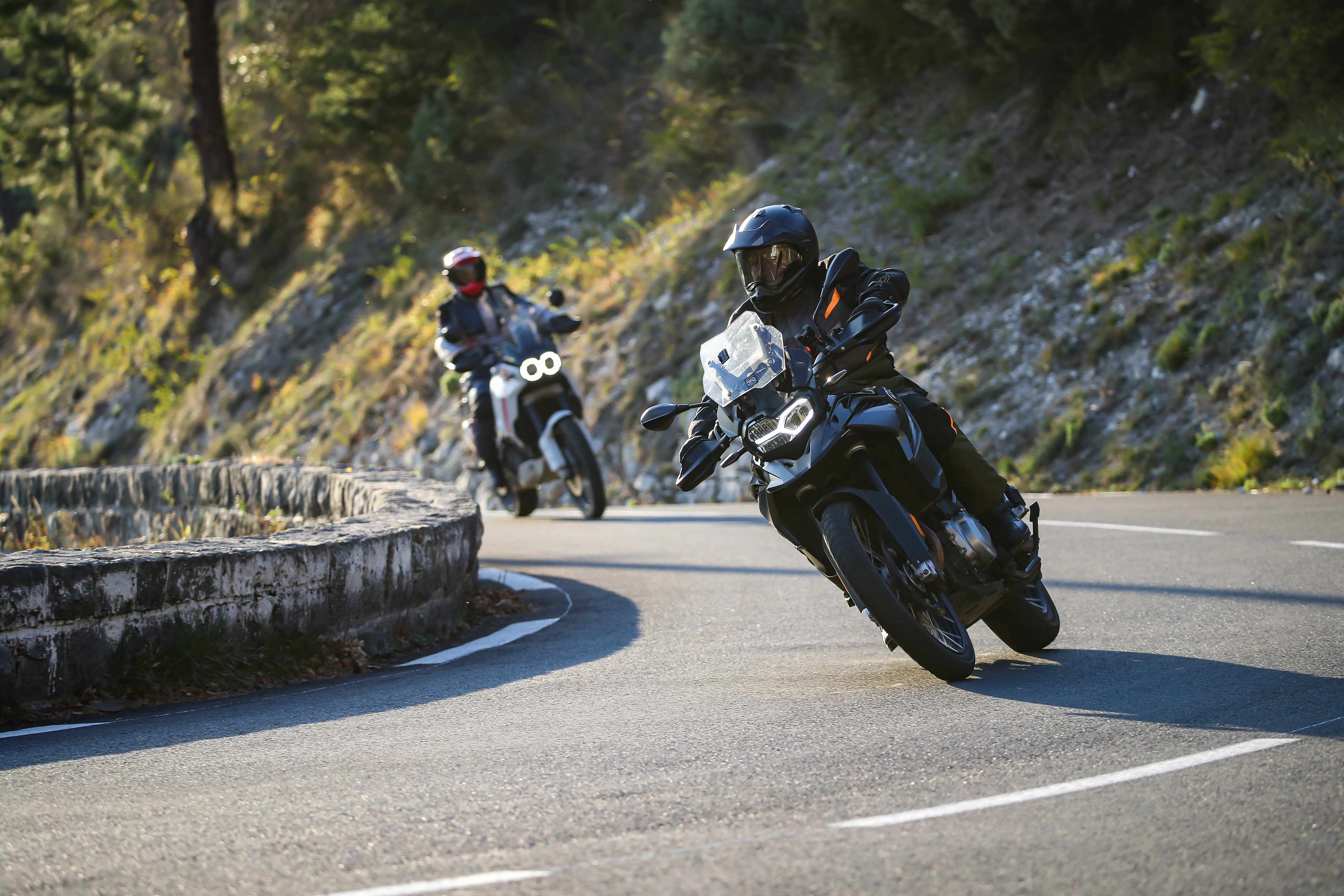 two people riding motorcycles down a curved road