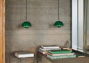 Two signal green Flowerpot VP10 pendant lamps hang over a textured concrete wall. Below, stacks of books, rest on a concrete ledge and a metal wire stand.