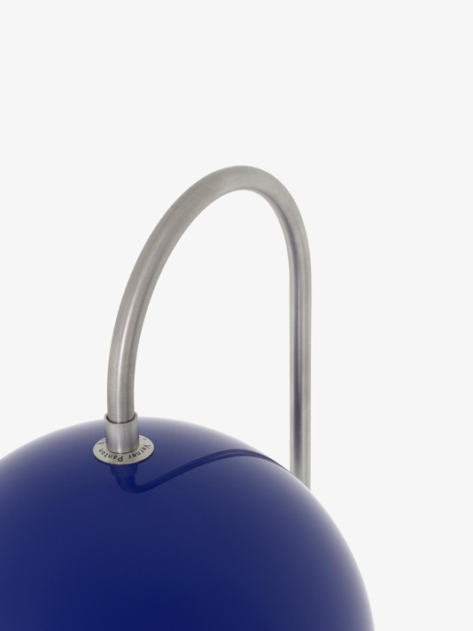 Close-up of a cobalt blue Flowerpot VP12 floor lamp's dome shade, showing the curved, brushed metal arm attachment and "Verner Panton" subtly debossed on the shade.
