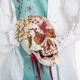Product A Holiday Company Animated Light-Up 5 Ft. 2" Standing Shaking Headless Skeleton Doctor Halloween Decoration, featuring a chilling skeleton with glowing red eyes, blood splatters, and a disturbing appearance for Halloween decor.