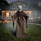 Morris Animated 7 Ft. 9" Light-Up The Time Demon Halloween Decoration, a tall, fearsome demon figure with a skull face, horns, glowing eyes, and outstretched clawed hands, standing in a haunted house yard decorated for Halloween.
