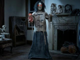 Morris Maniac Mary in a Straitjacket with Doll Halloween Decoration - 5 Ft. - Haunted Halloween themed mannequin with glowing red eyes, wild black hair, and distressed clothing, holding a creepy doll, in a decorated spooky room.