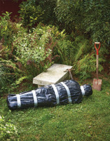 Fun World Body In A Bag- 5' , outdoor garden scene with a black body bag, garden tools, and plants.