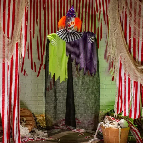 Product A Holiday Company Light-Up 6 Ft. Hanging Clown with Sound Halloween Decoration, spooky clown with orange hair, painted face, purple hat, and striped costume hanging in a haunted circus or carnival scene.