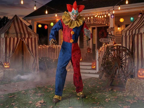 Morris Animated 7 Ft. 3" The Axe-Wielding Clown Halloween Decoration, a large, menacing clown in colorful costume wielding an axe in front of a spooky haunted house with Halloween decorations and pumpkins.