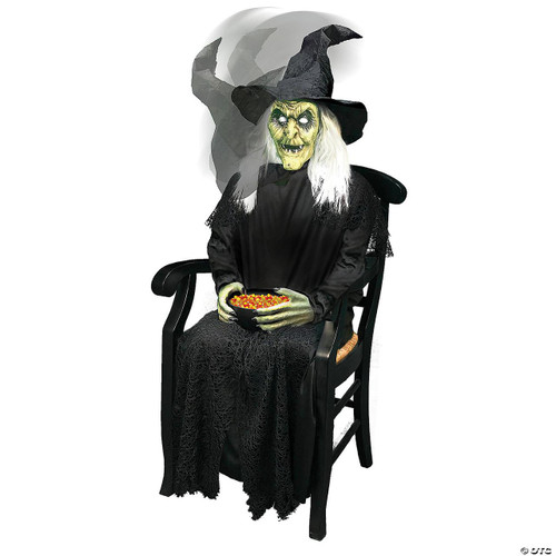 Morris Sitting Witch Animated, a Halloween-themed ghostly witch decoration with a green face, long white hair, black hat, and black dress, sitting on a black chair holding a bowl of colorful candy.