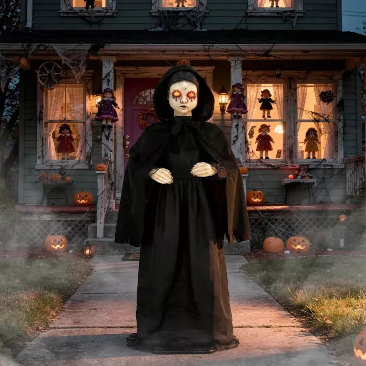 Morris Animated 5 FT Light-Up LED Standing Doll with Moving Head & Eyes, Halloween decoration featuring a spooky doll in a black hooded cloak with glowing eyes in front of a haunted house decorated for Halloween.