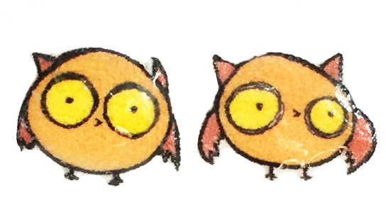 Small handmade owl stud earrings featuring round orange-brown owls with large yellow eyes and simple expressive faces on a clean background.
