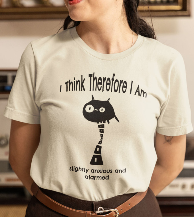 Close-up of philosophical monster illustration inspired by Descartes with humorous existential quote on tan tee.