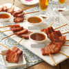 Bacon lollipop sampler serving arrangement with skewered bacon and several dipping sauces.