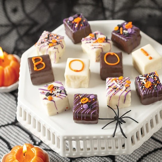These hand-decorated, Halloween-themed delights may be bite-sized, but they bring full-sized charm. Each miniature cake layers moist, decadent sponge with smooth, velvety filling, then seals it all in a rich chocolate shell adorned with cheerful “Boo” designs.