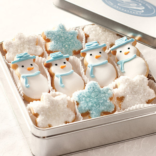 Iced snowman cookies with blue hats and scarves beside blue and white snowflake cookies in an open metal gift tin