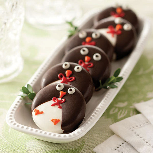 Chocolate-covered penguin cookies with white faces and orange beaks arranged on a platter.