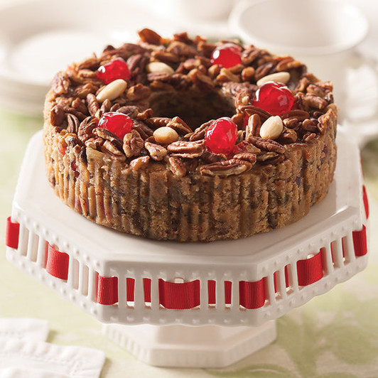 Fancy fruit cake in a ring shape topped with red cherries, pineapple, raisins and nuts.