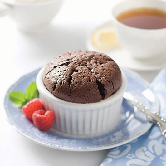 Baked chocolate soufflé in a white ramekin on a blue plate beside raspberries.