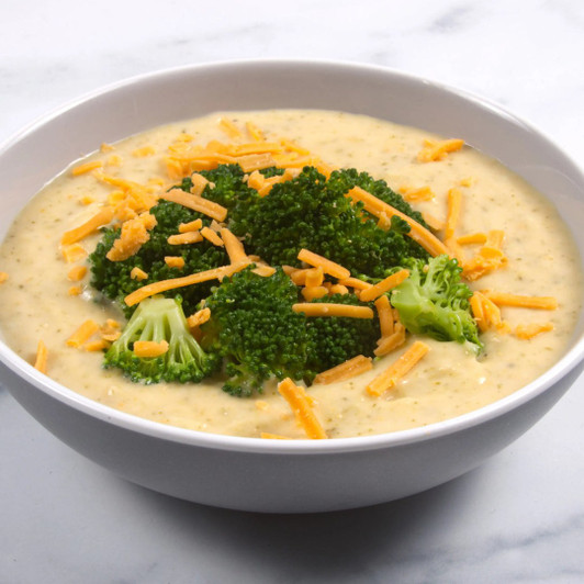 Bowl of creamy broccoli and cheddar soup topped with broccoli florets and shredded cheddar