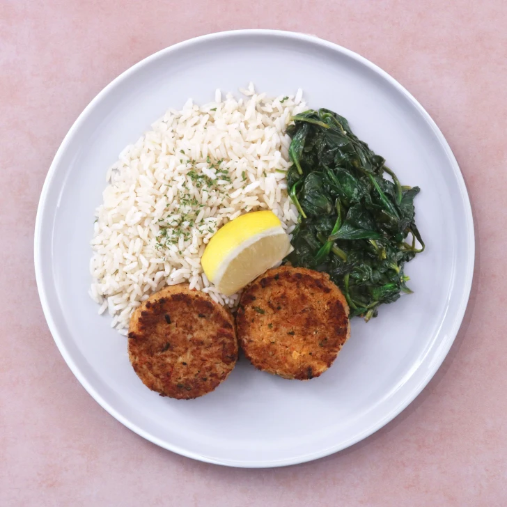 Prepared crab cakes dinner with seasoned crab cakes, white rice, and sautéed spinach.