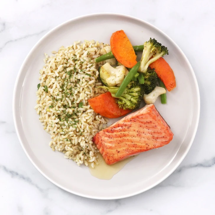 Prepared seared salmon dinner with brown butter sauce, brown rice, and roasted vegetables.